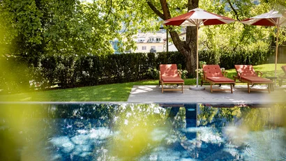 Pool mit roten Liegestühlen und Sonnenschirmen unter Bäumen im Garten