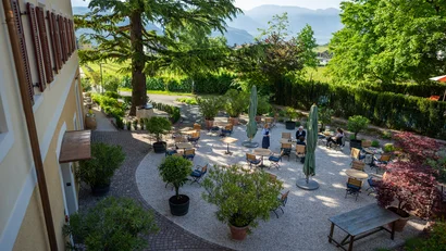 Gartenrestaurant mit Tischen, Stühlen und grüner Umgebung bei Sonnenschein