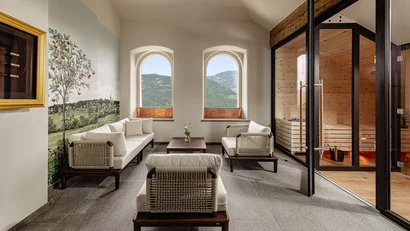 Heller Warteraum mit Sofa, Sesseln, Fensterblick auf Berge und Holzsauna