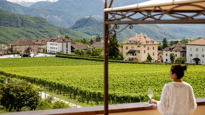 Frau blickt auf einen grünen Weinberg mit Bergen und Häusern im Hintergrund