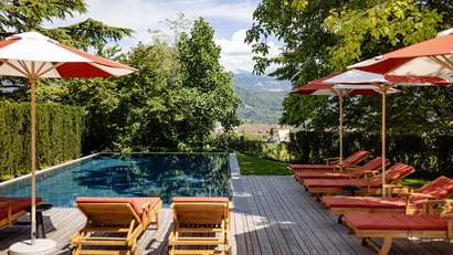 Poolbereich mit Liegestühlen und Sonnenschirmen in einem grünen Garten