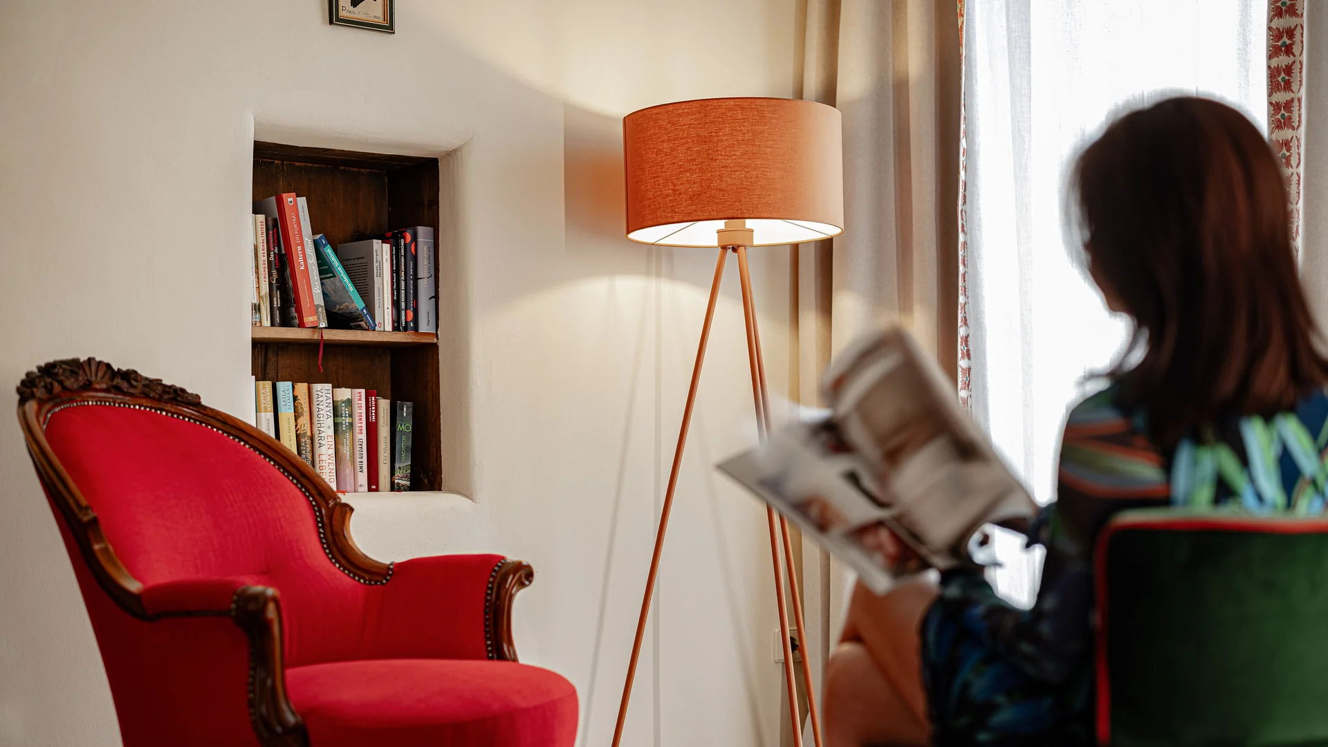 Frau liest in gemütlichem Raum mit rotem Sessel und Stehlampe