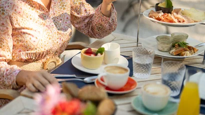 Frau genießt Frühstück mit Kaffee, Saft und kleinen Snacks im Freien