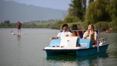 Paar entspannt auf Tretboot auf ruhigem See mit Paddler im Hintergrund