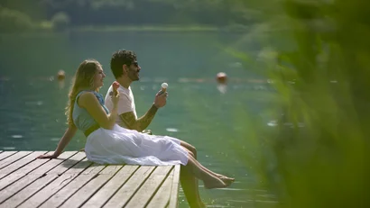 Paar sitzt am Steg und isst Eis am See an einem sonnigen Tag
