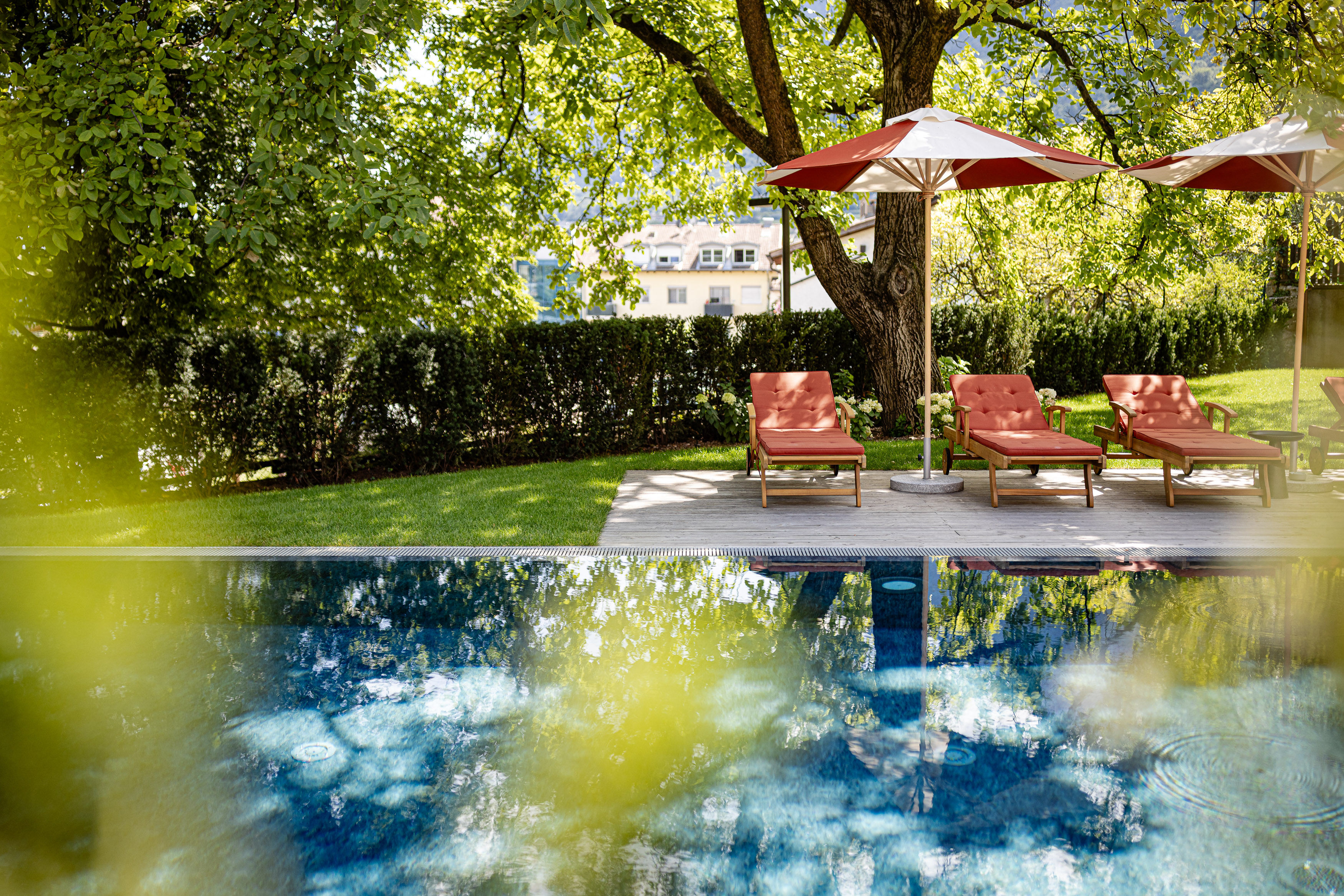 Pool mit roten Liegestühlen und Sonnenschirmen unter Bäumen im Garten